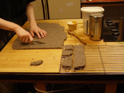 Me cutting a strip off the flattened dough with a knife. Nearby, there is a rack with some other strips of dough sitting on it.