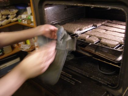 The same rack of biscuits being put into an oven, using potholders.