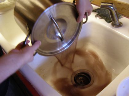 Me holding lid on the pot, while I pour brownish water from it into the sink. (The water goes through the thin gap between the pot and the lid, so none of the beans come out.)