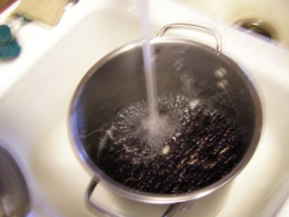 The pot full of beans sits in the sink, with tapwater pouring into it.
