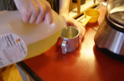 Me pouring canola oil from a 1-gallon bottle into a metal 1-cup measure.