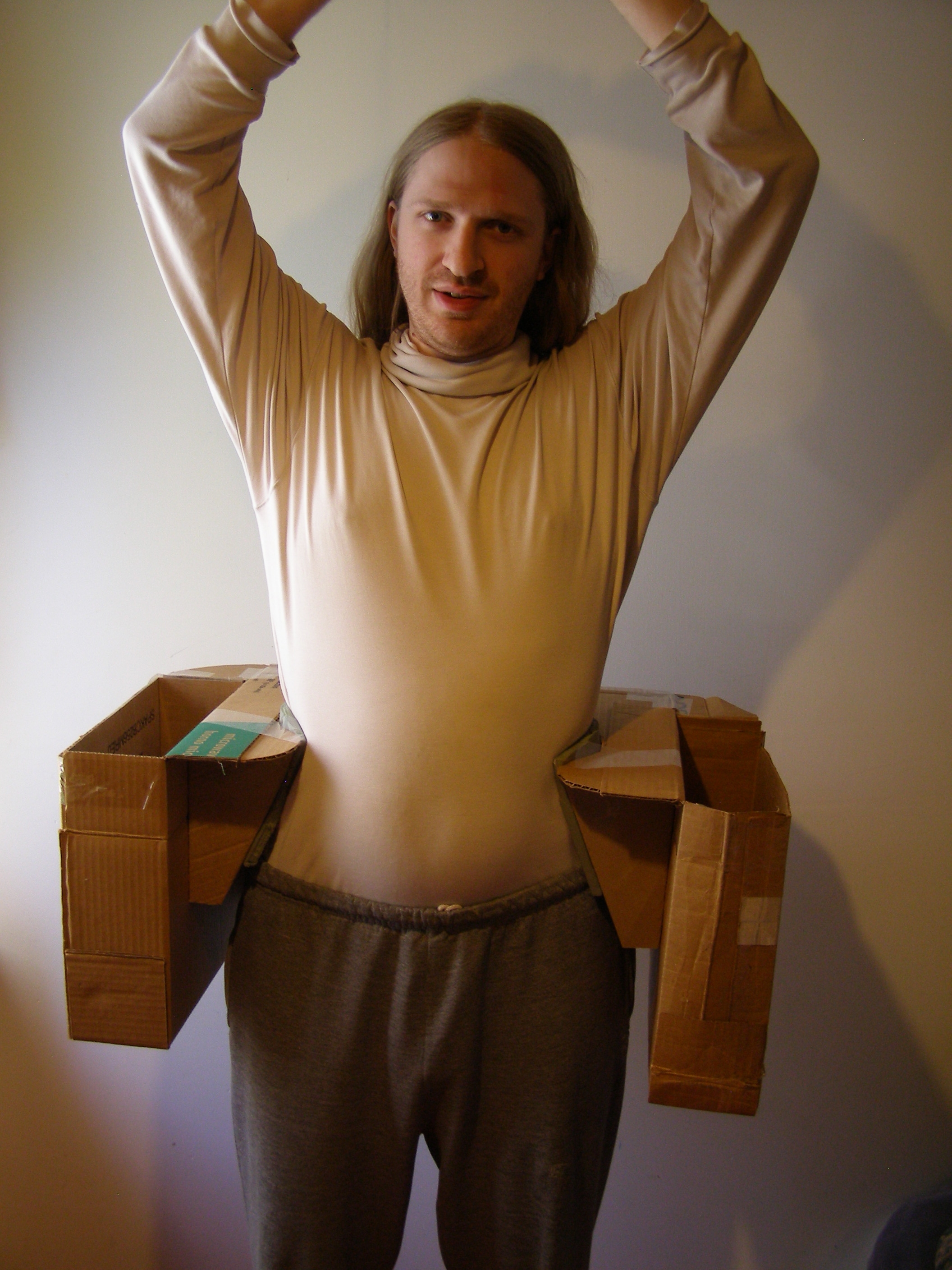 [Photo: Me, wearing Saddlebags 2.0 around my hips. They are a rectangular-ish cardboard contraption that supports two cardboard boxes at my sides.]